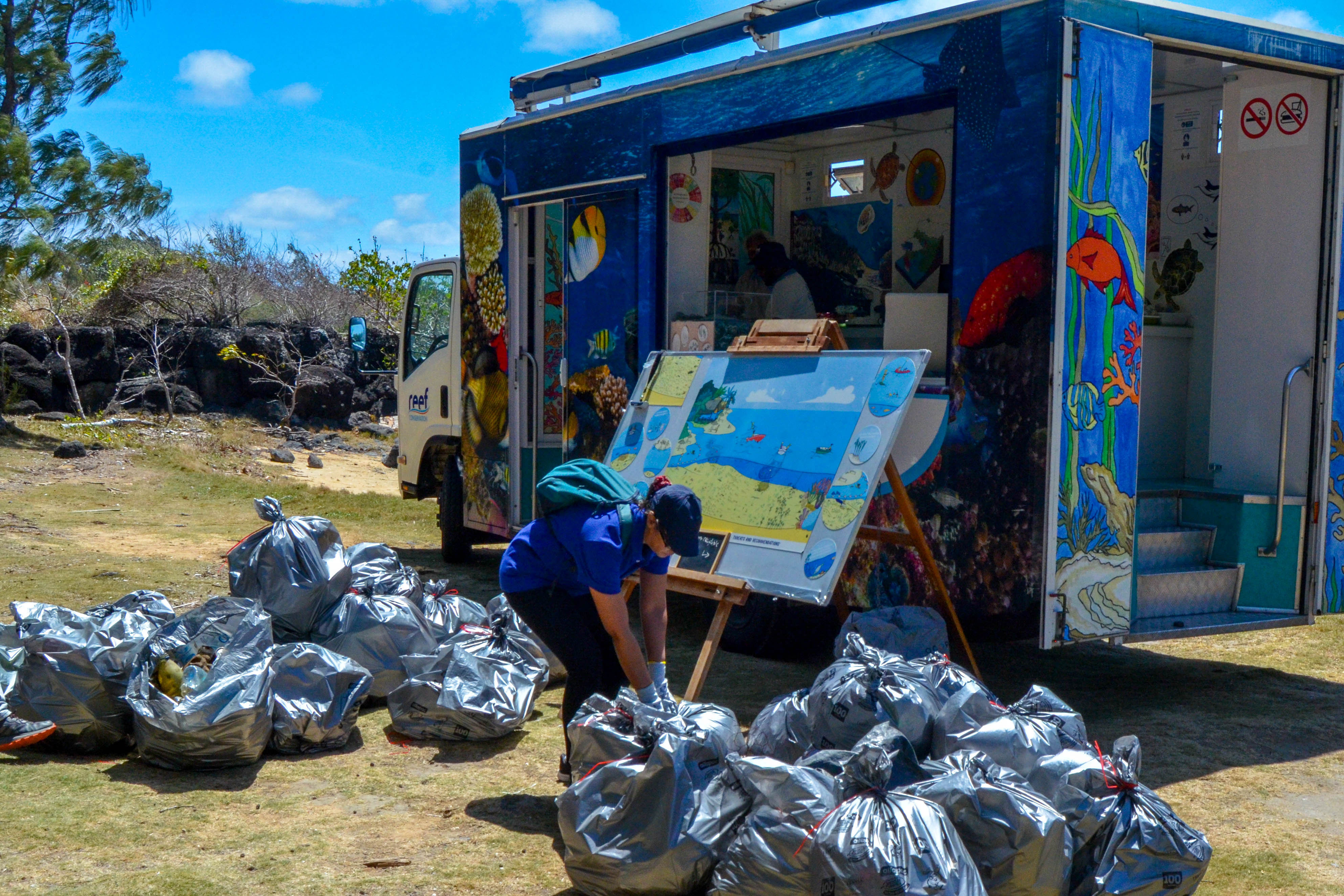 2024 EUBeachCleanup in Mauritius, one person in front of a truck and many grey plastic bags filled with rubbish